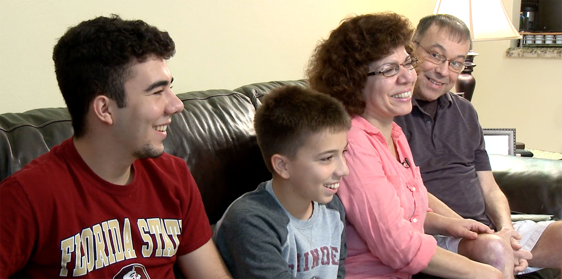 Family of 4 happily sits on couch. Dad is sarcoma survivor