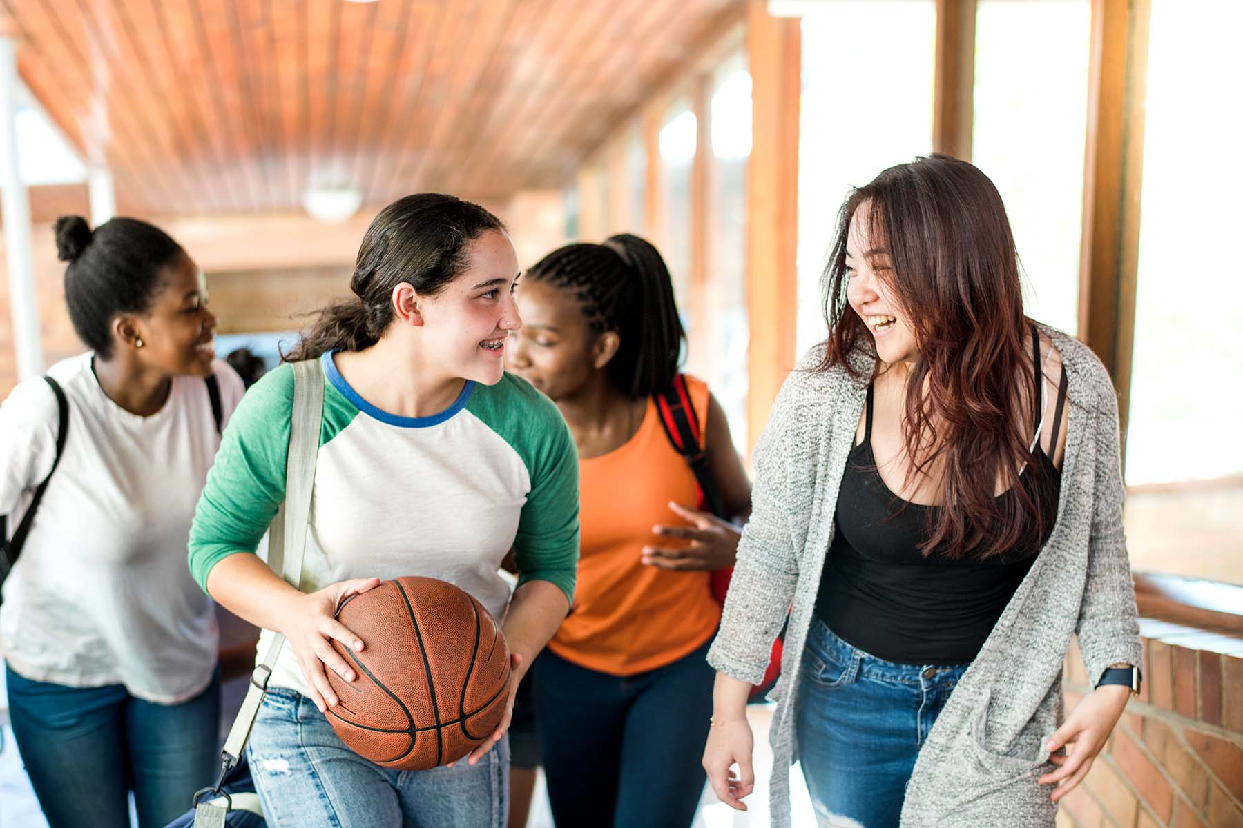 Four multiethnic female friends walk in outdoor hallway at school