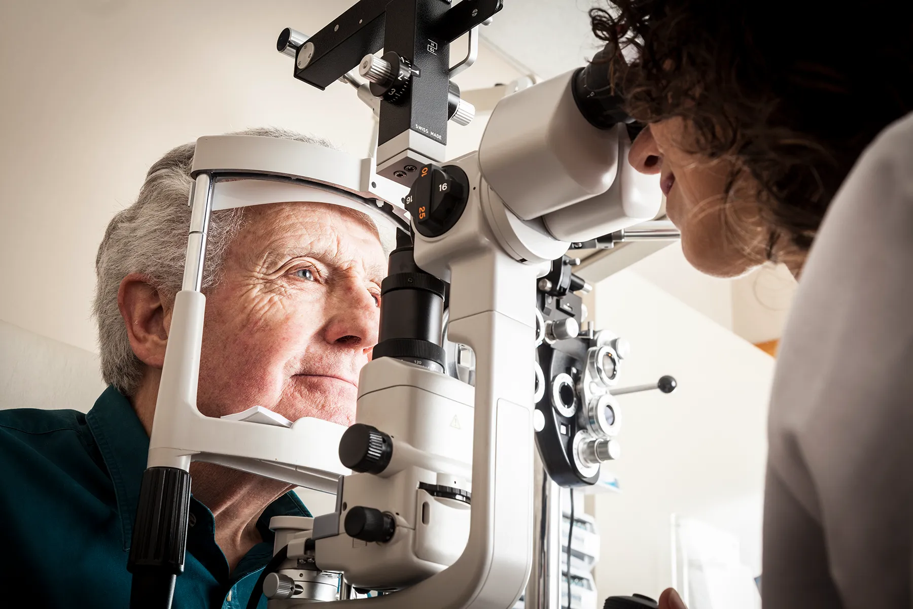 An optometrist examines a senior man's eyes using a large ophthalmic examination machine in a clinic.