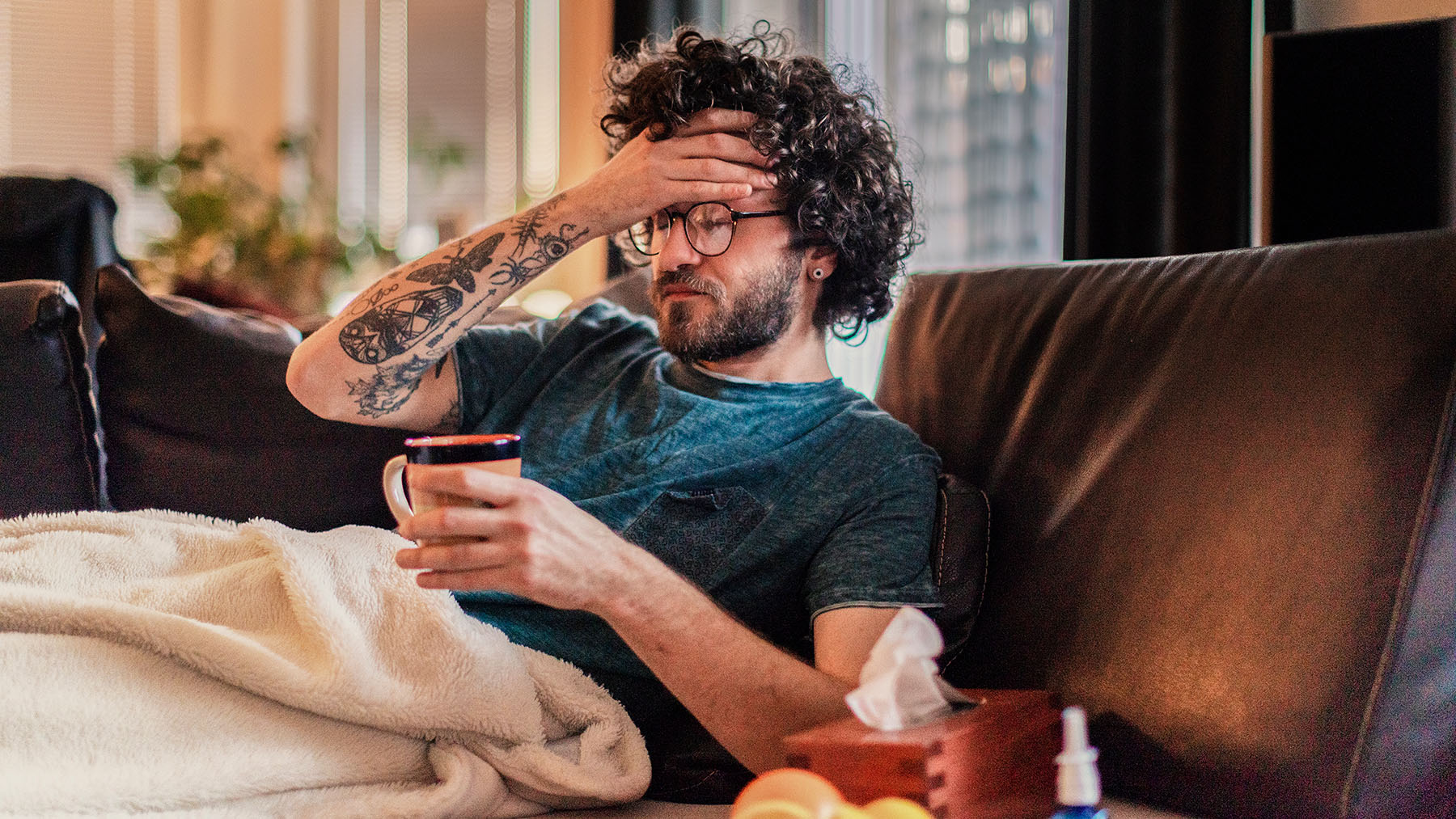Man with tatooed arm feels sick on couch
