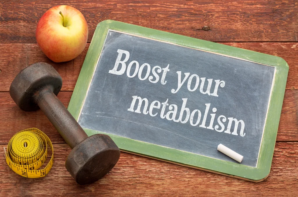 Chalkboard with "Boost your metabolism" message, alongside a dumbbell, apple, and measuring tape, representing health, fitness, and weight loss.