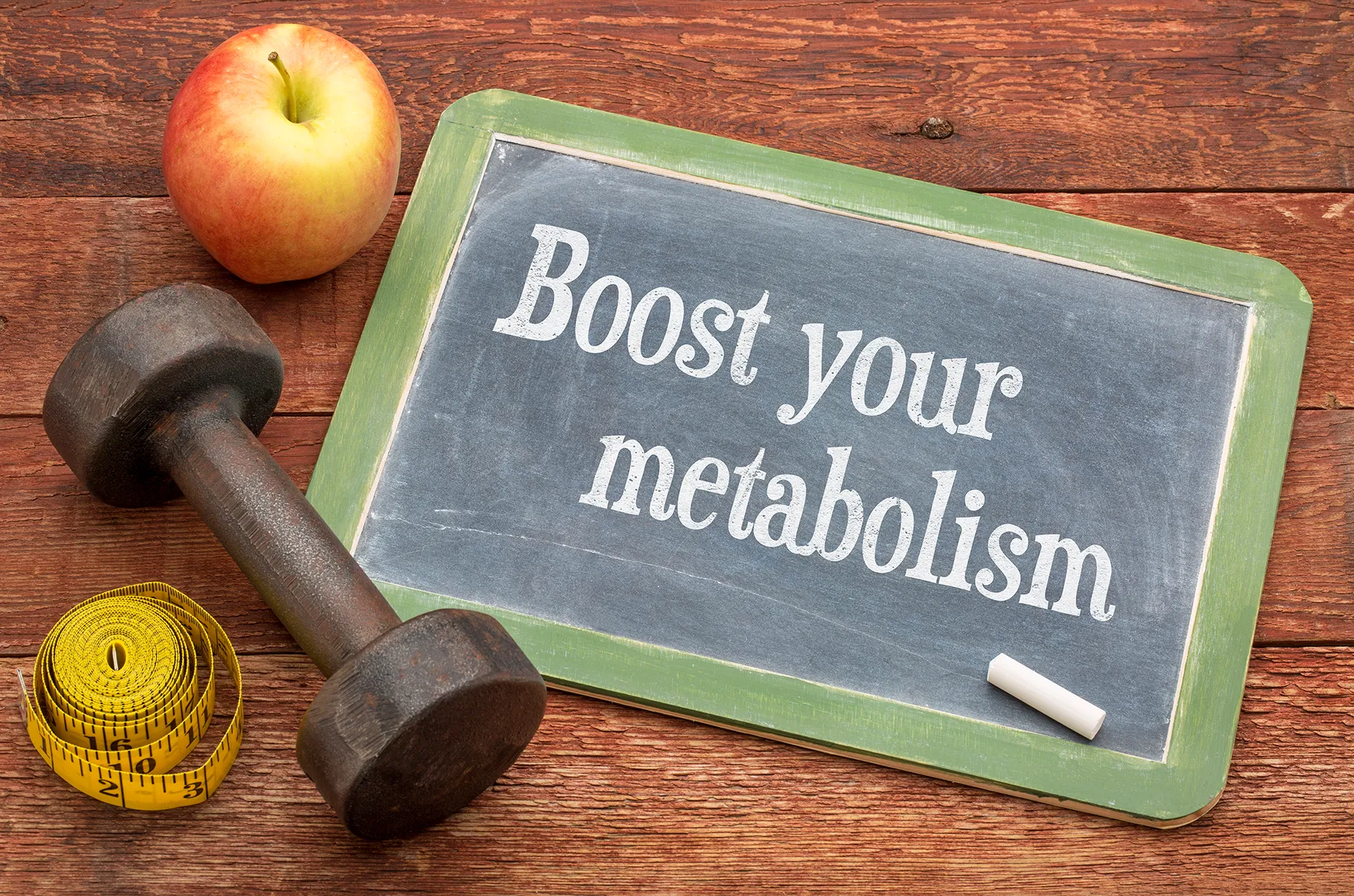Chalkboard with "Boost your metabolism" message, alongside a dumbbell, apple, and measuring tape, representing health, fitness, and weight loss.