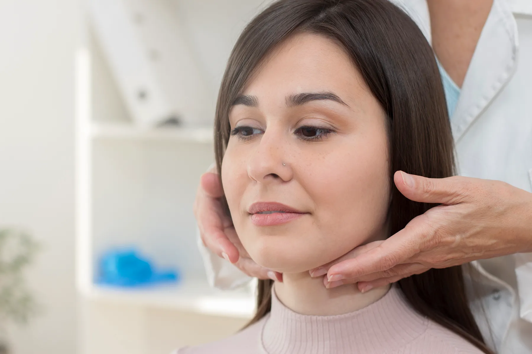 Medical professional examining a young woman's neck.