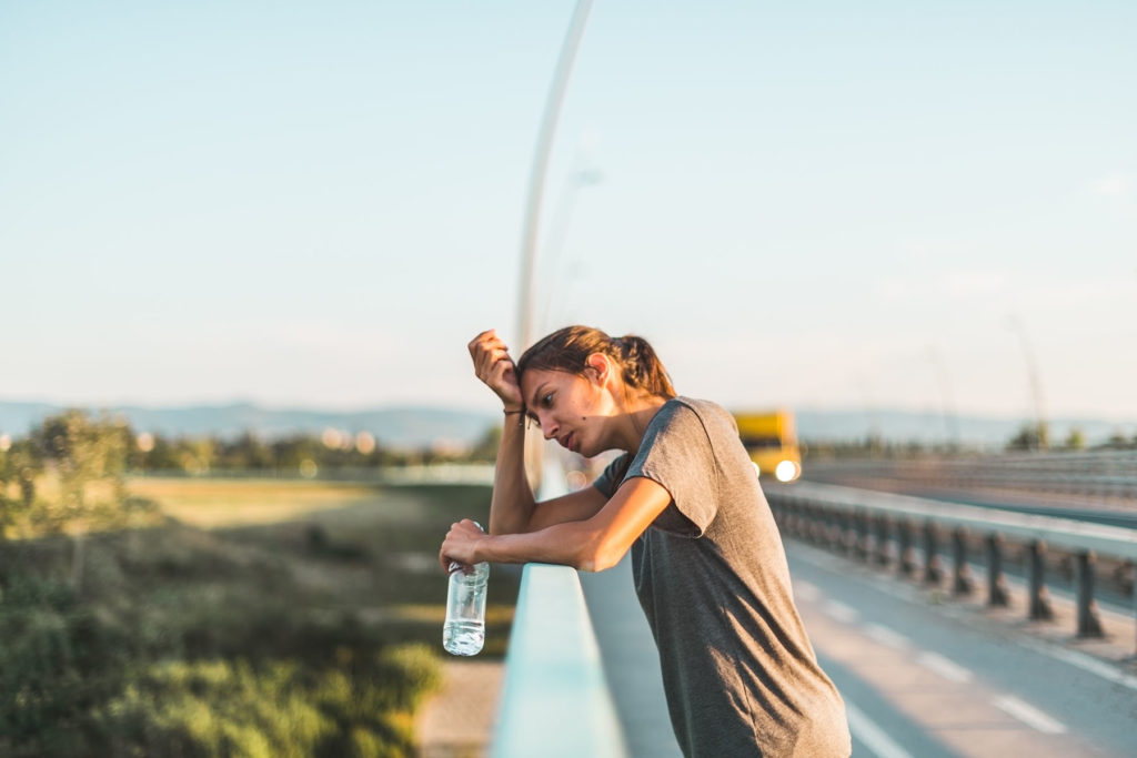 Overheated female runner rests on guardrail to take a water break.