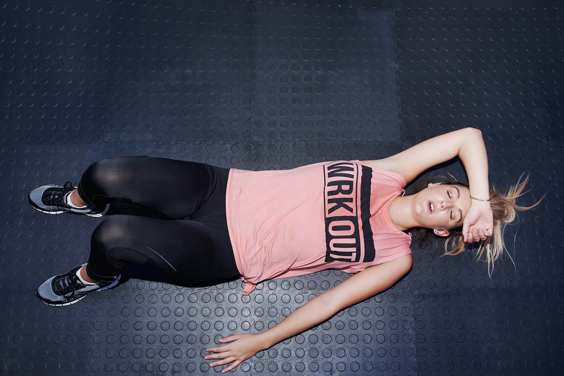 Woman lays on gym mat, exhausted and sweaty