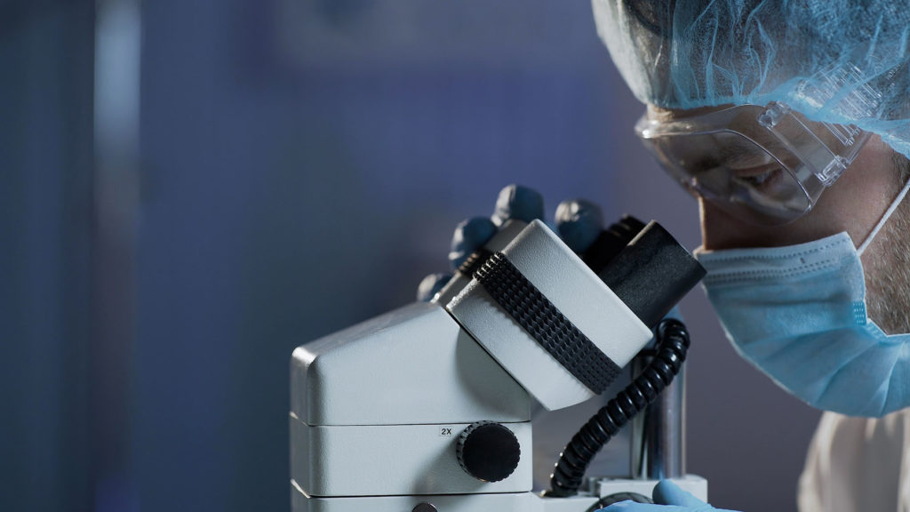 Researcher with goggles looking closely through microscope