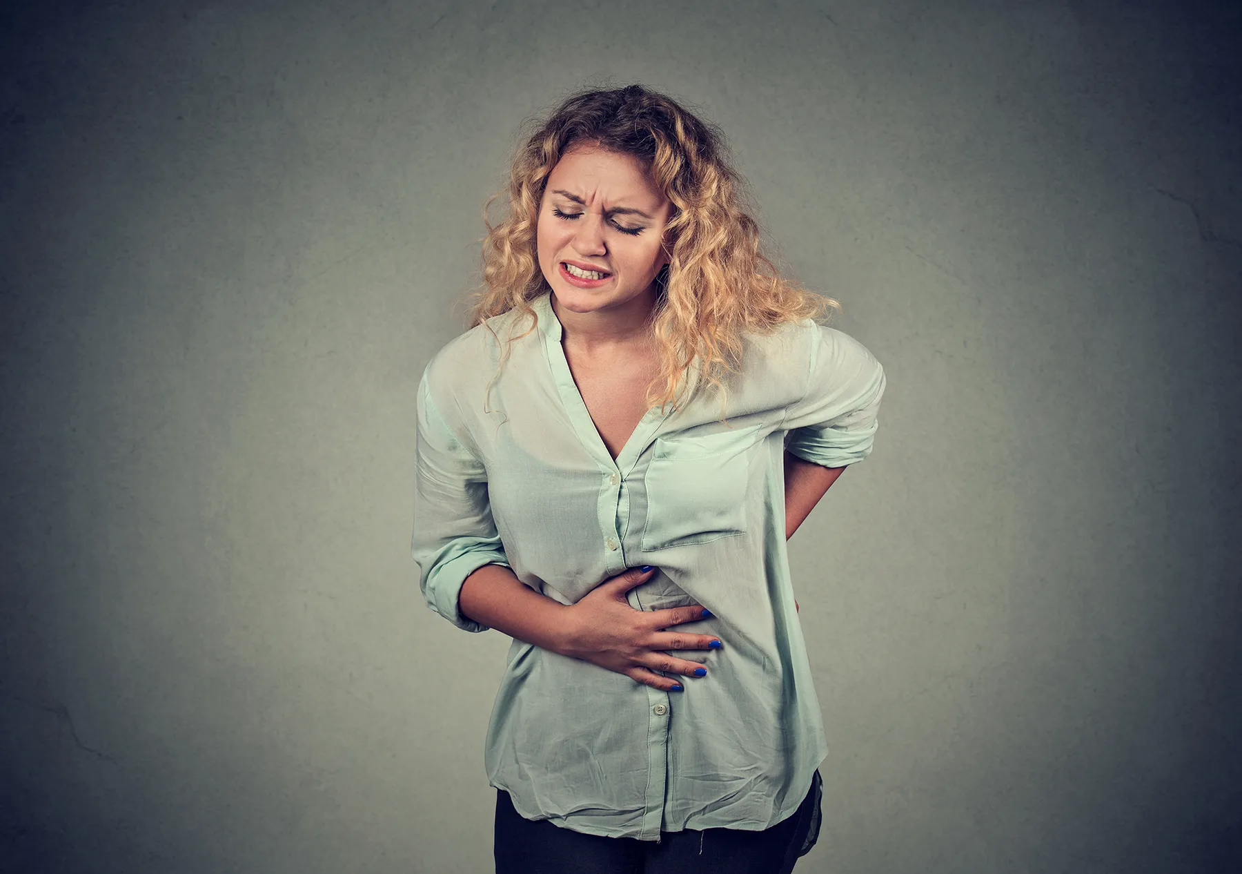Woman grimacing from severe stomach and lower back pain, clutching her abdomen and back.