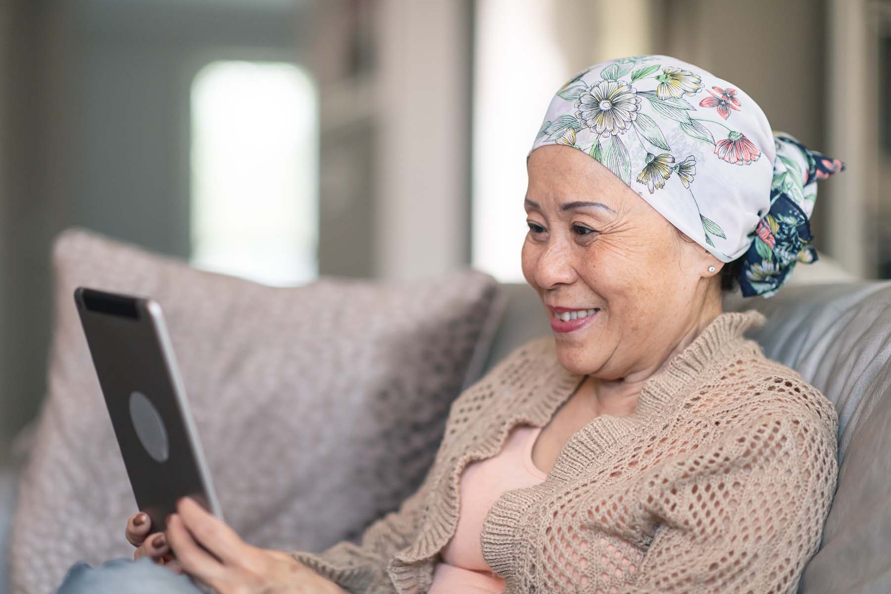 Older Asian cancer patient smiles at tablet
