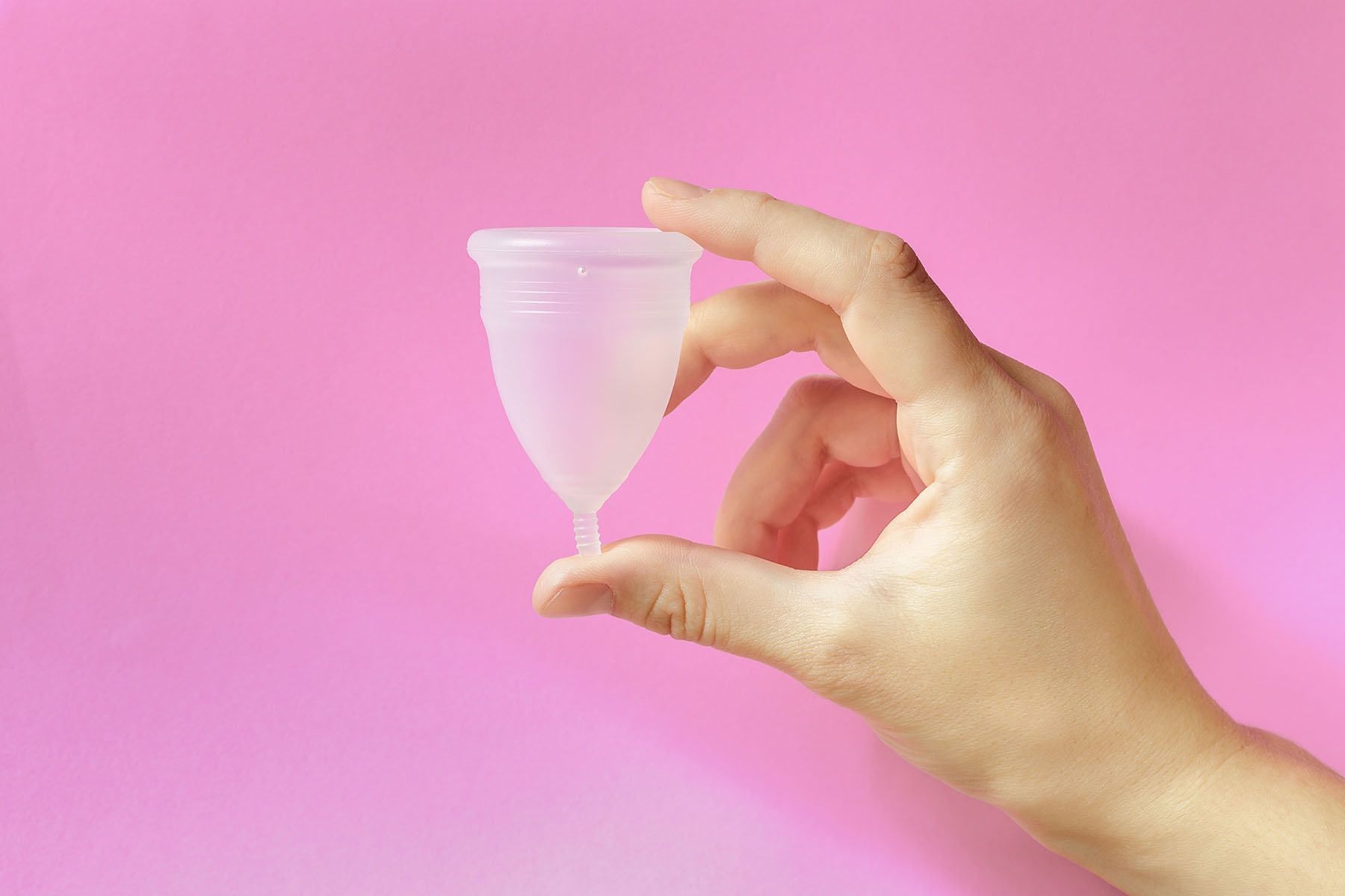 hand holds menstrual cup against pink background