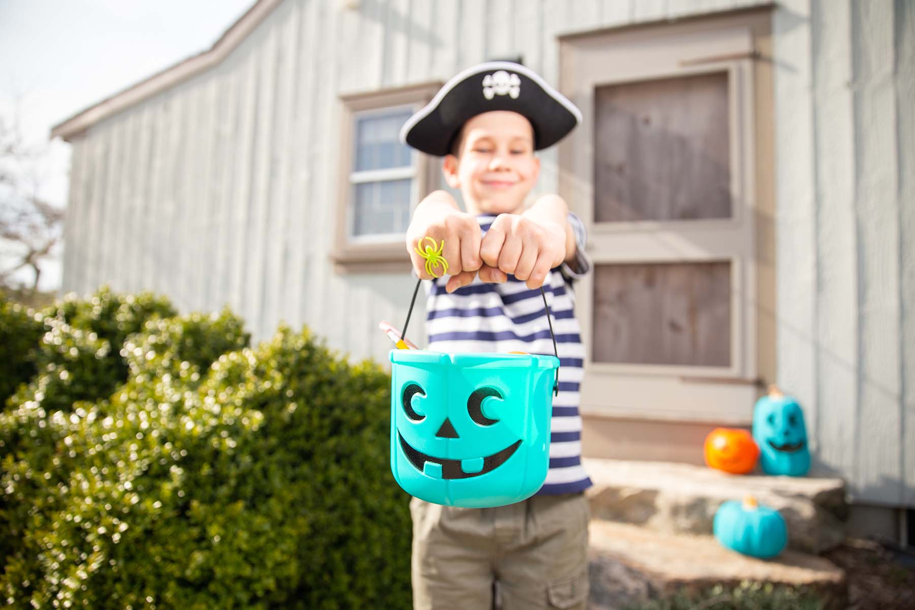 Boy in pirate hat holds teal Halloween pumpkin out. Teal shows that the child has food allergies.