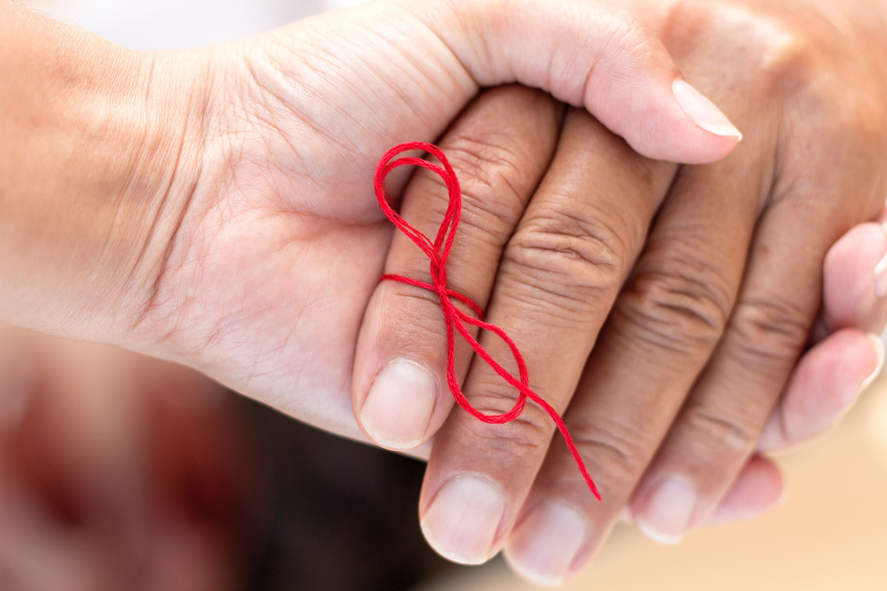 two hands with red ribbon tied around fingers
