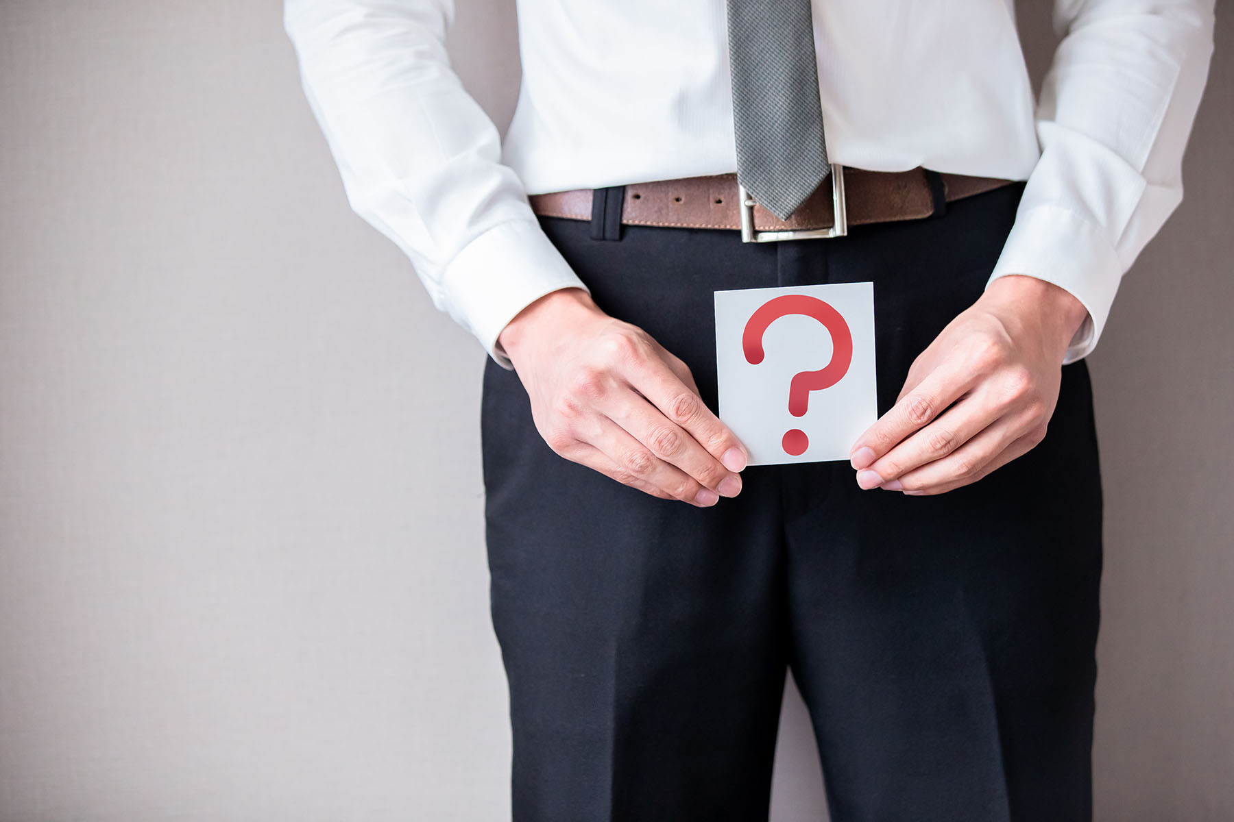 Man in business attire holds question mark sign over his pelvic area