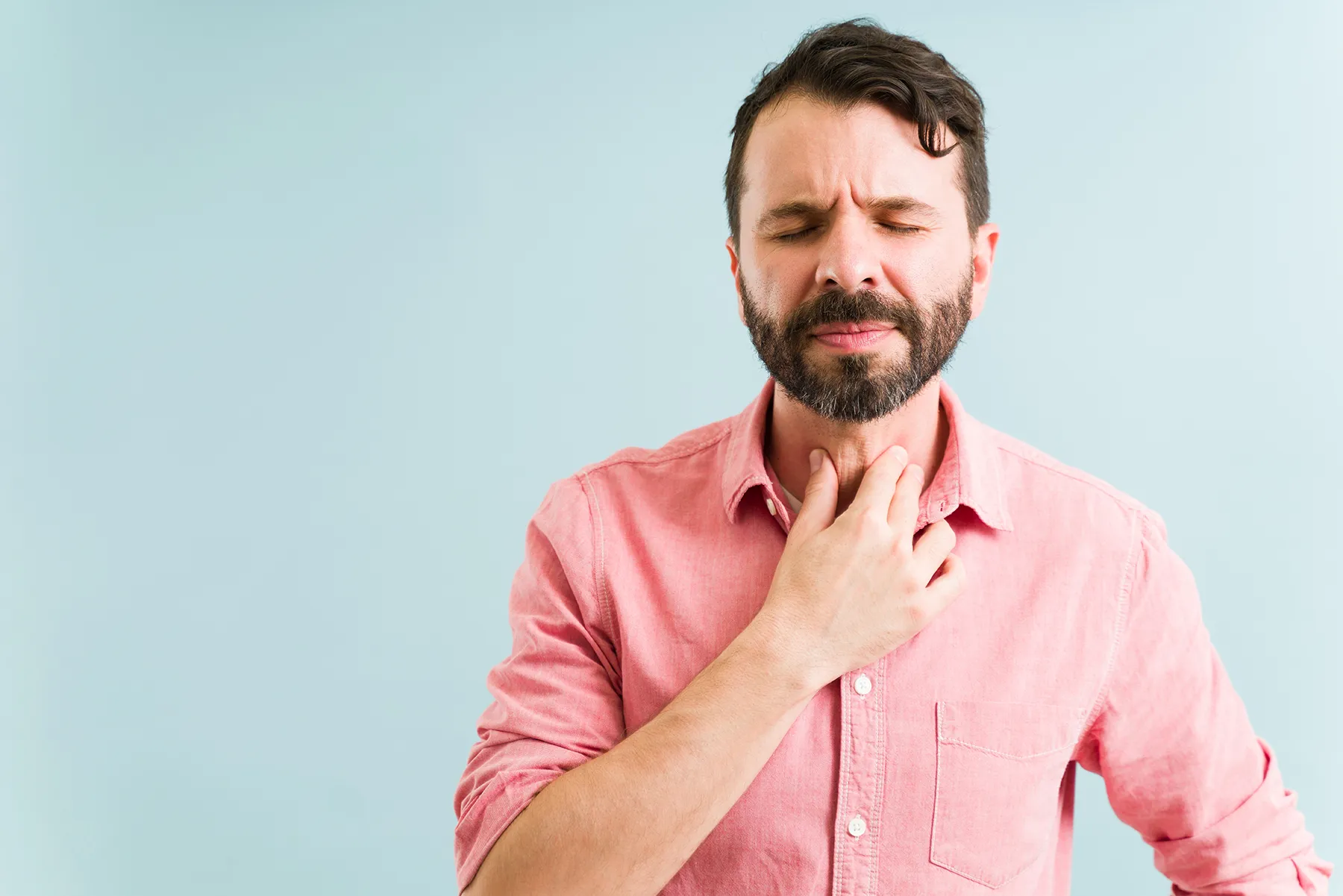 Man holding his neck with a pained expression and closed eyes, indicating a sore throat or discomfort.