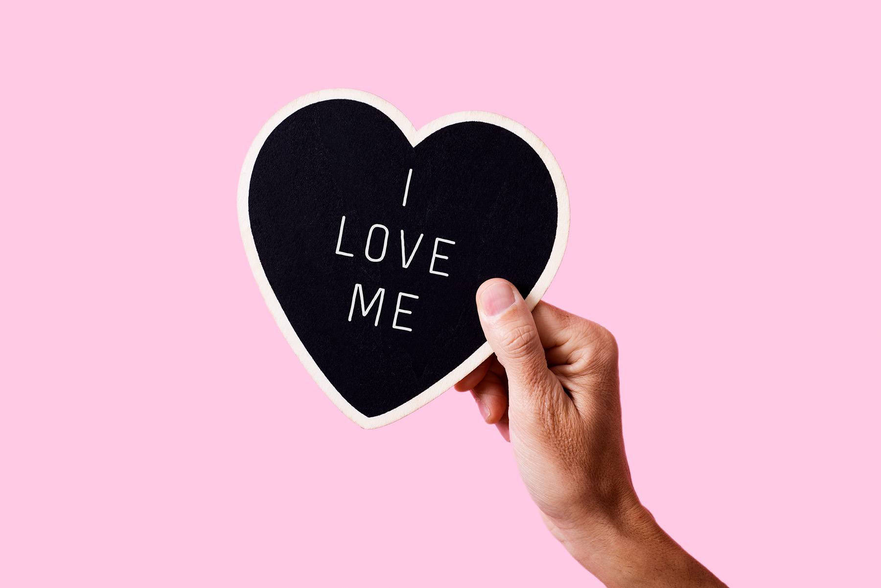 Hand holds up sign that says I Love Me against pink background