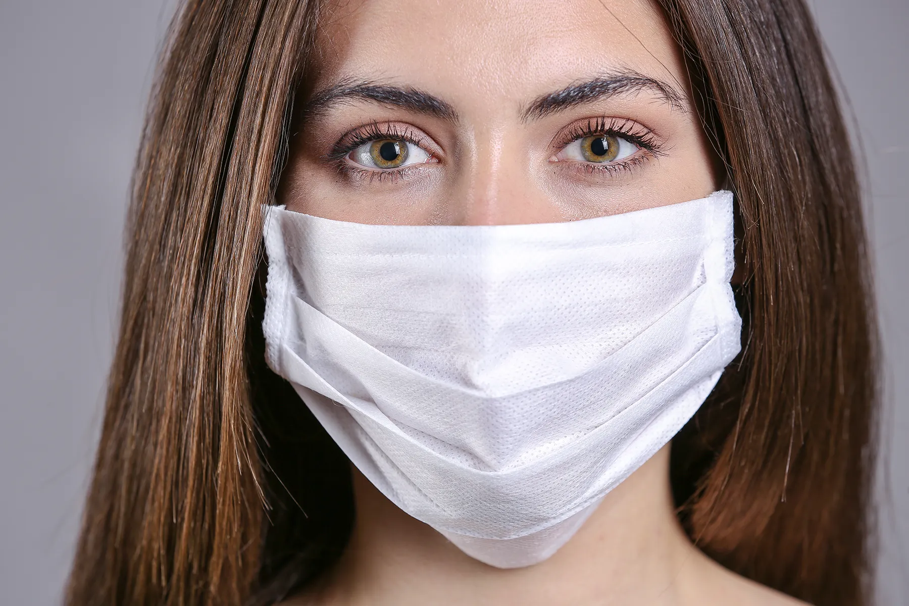 Close-up portrait of a woman with hazel eyes wearing a white medical face mask.