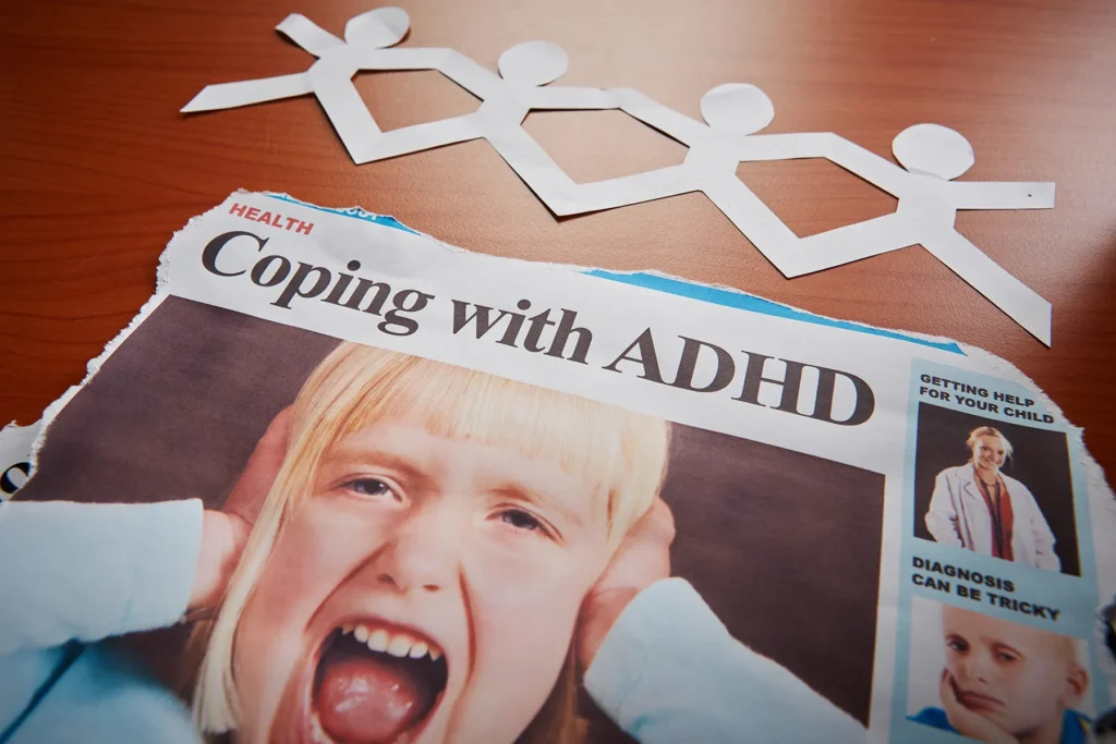 Newspaper headline "Coping with ADHD" featuring a distressed child covering their ears, with a chain of paper people above symbolizing support, and articles on child diagnosis and getting help.