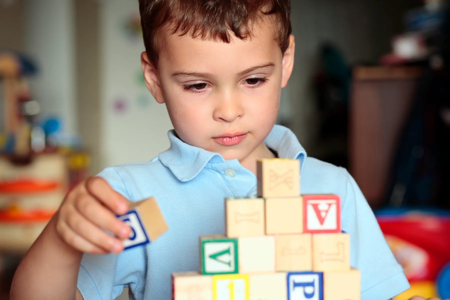 Focused young boy in a blue polo shirt stacking colorful wooden alphabet and number blocks to build a tower.