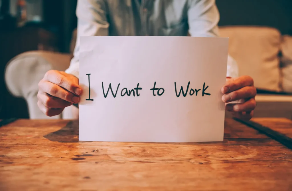 Hands holding a sign that reads 'I Want to Work' on a wooden table, symbolizing job searching, unemployment, or the desire for work.