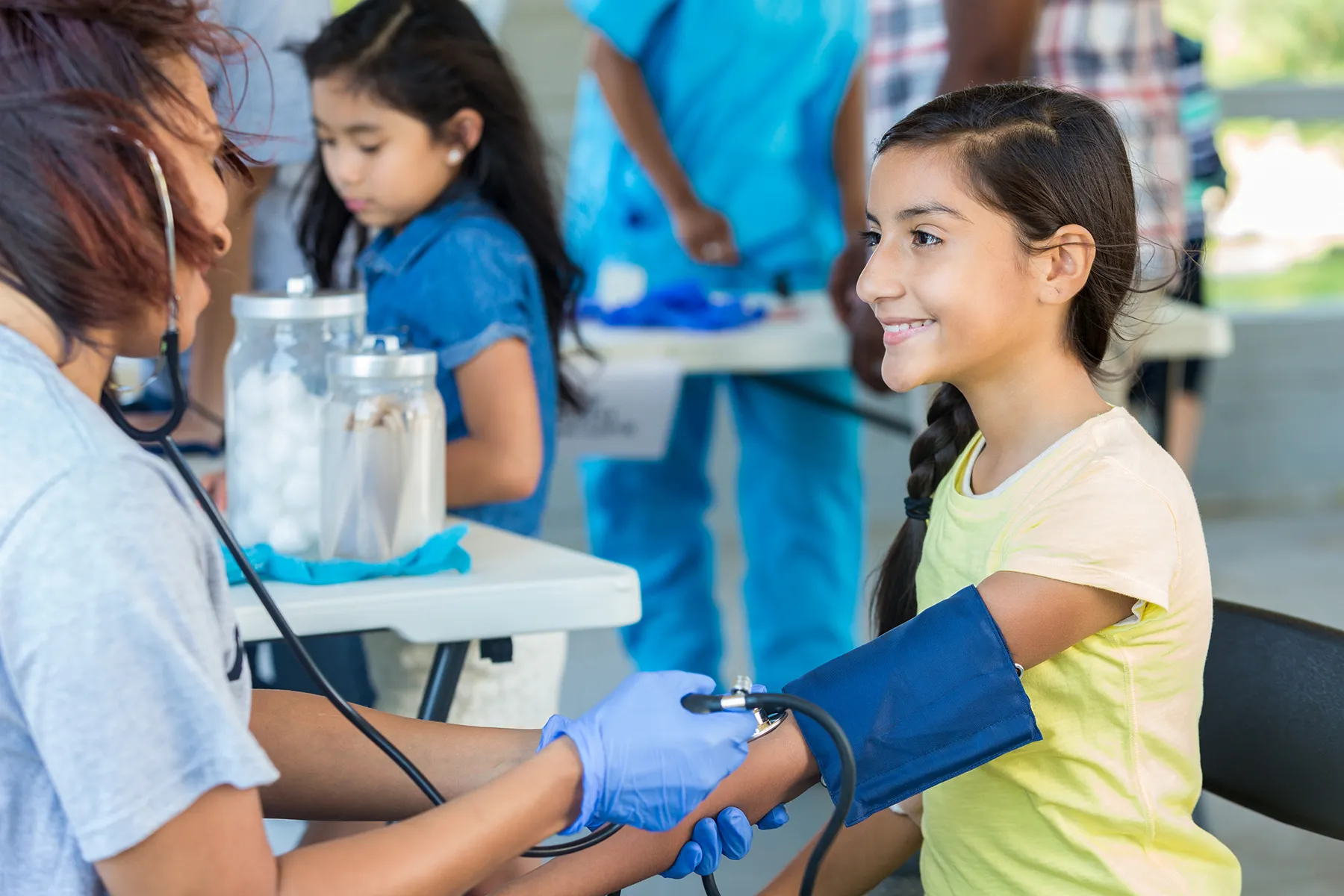 Smiling young girl having her blood pressure taken by a medical volunteer at a community health screening event.