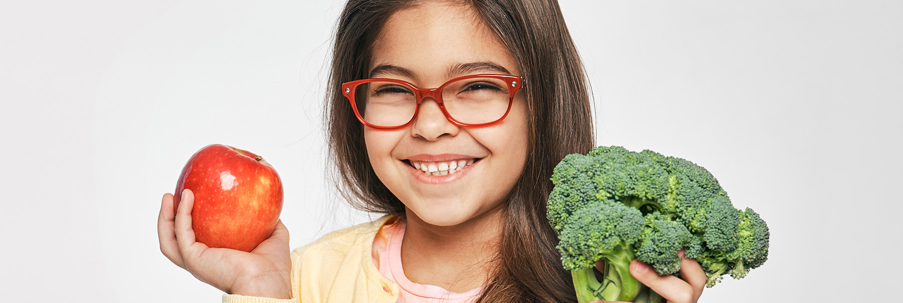 Cute young Hispanic girl holds tomato and broccoli