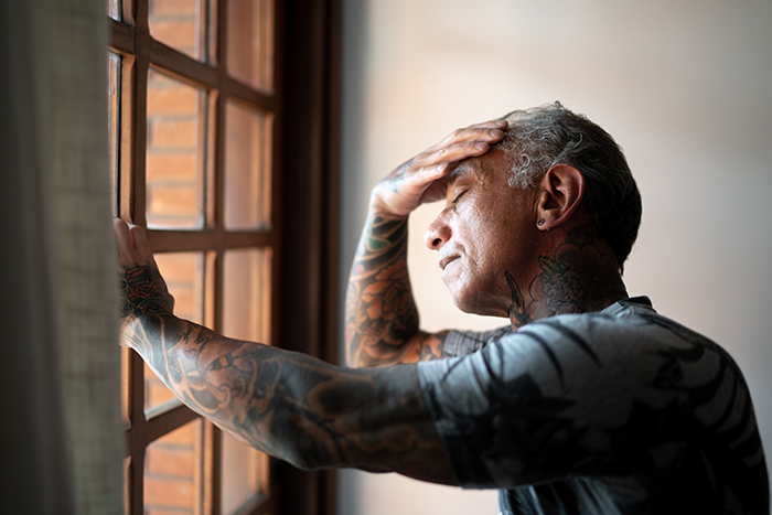 Fatigued older man leans against window
