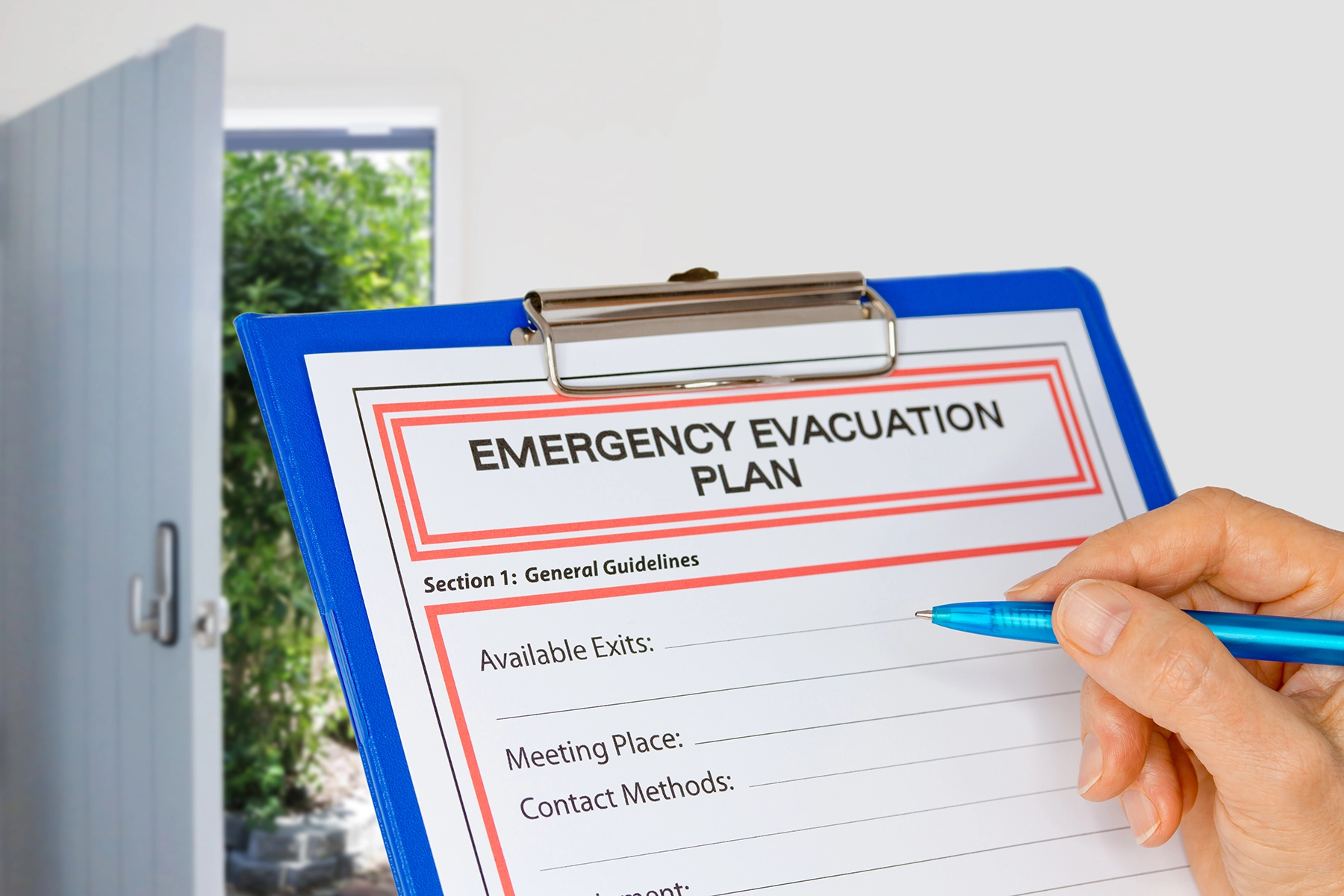 A hand fills out a family's emergency evacuation in case of fire plan on a clipboard.