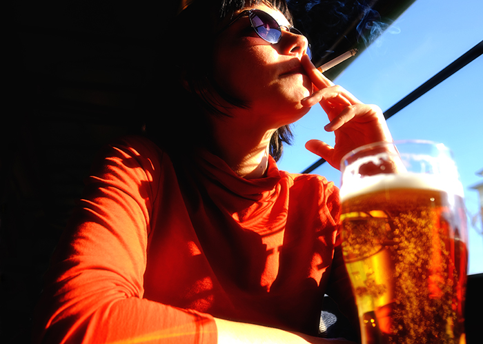 Woman smokes outside while drinking beer