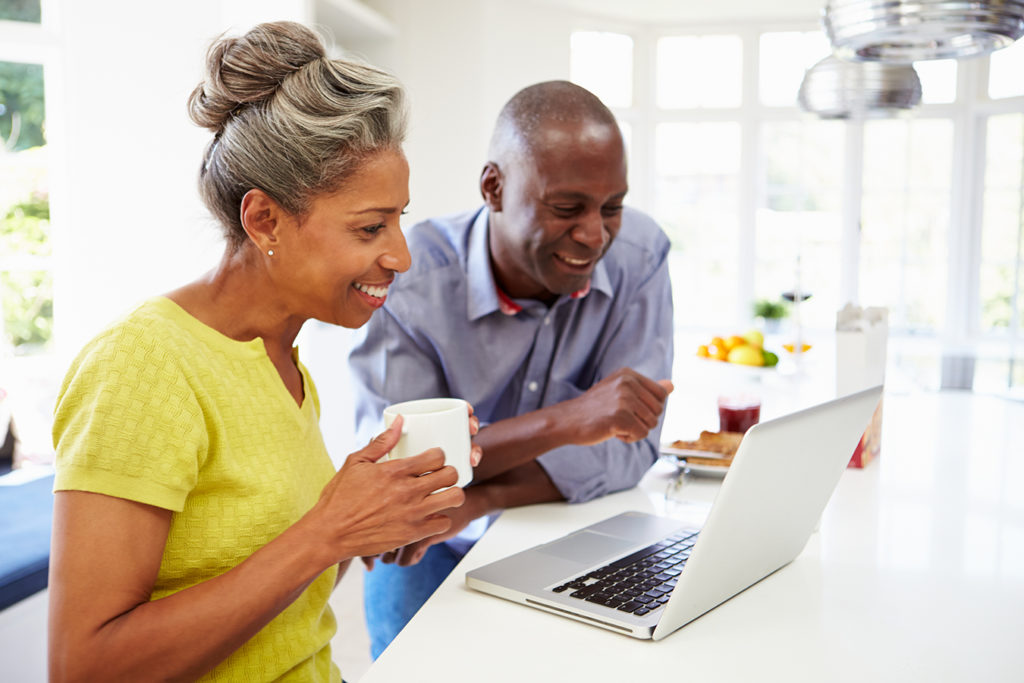 Mature Black couple drinks coffee while looking at a laptop