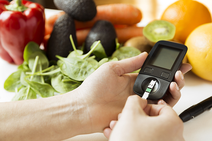 person using a finger stick for diabetes with veggies in background.