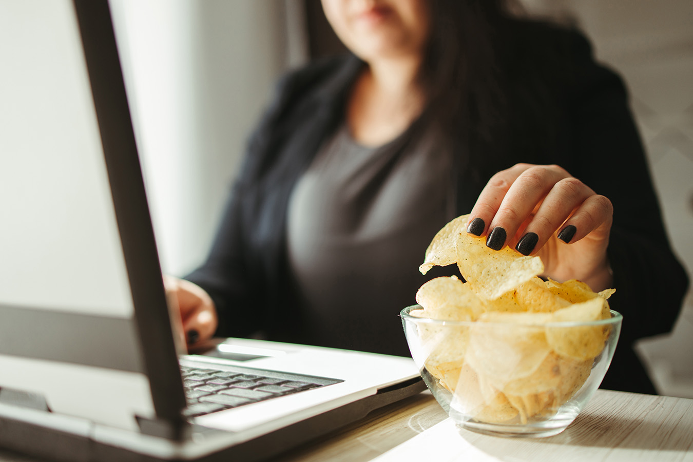 Woman mindless reaches for chips while at the computer.