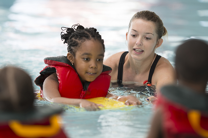 Little girl happily wears a life jacket during swim lessons.