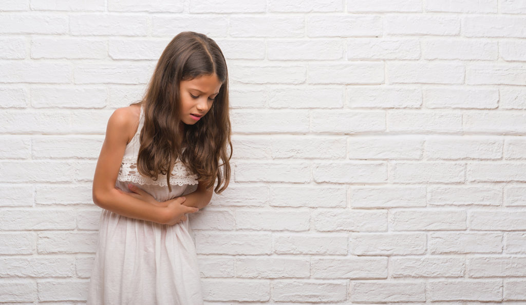 Young girl in white dress holds stomach in pain
