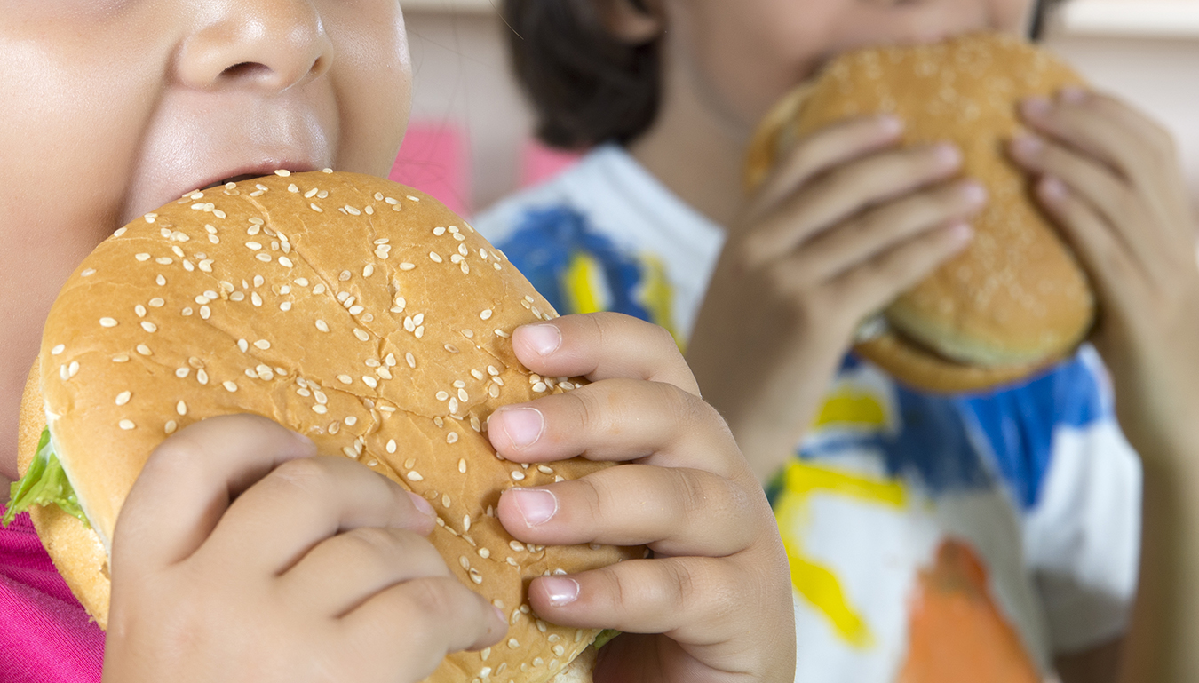 Close up of boy and girl eating big hamburgers.