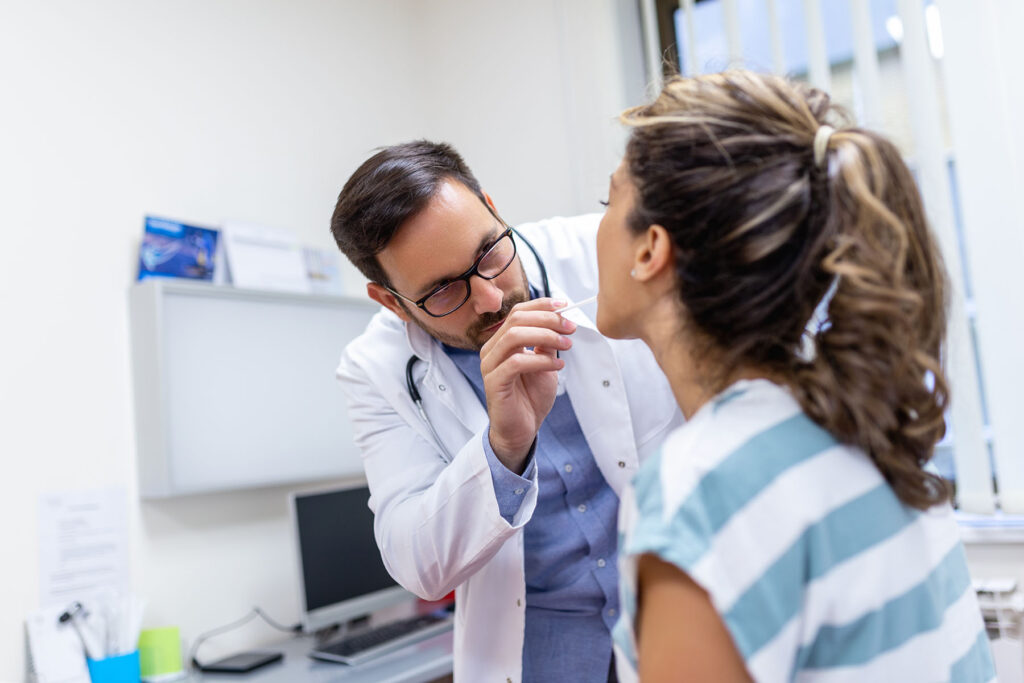 Doctor putting a tongue depressor into the mouth of a young female patient.