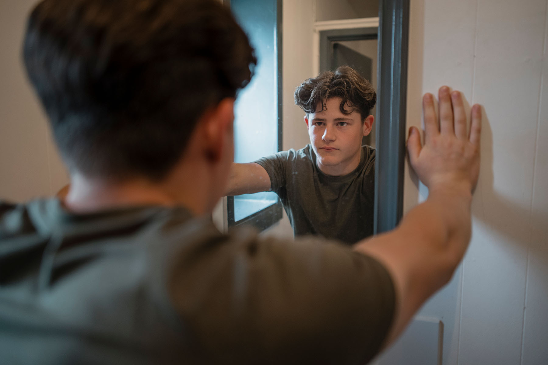 Teen boy looks frustrated, tired in mirror