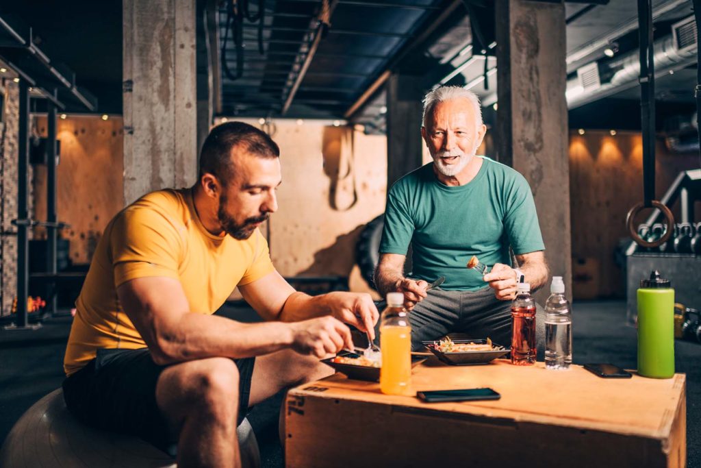 Two Hispanic men eating protein-rich salad after workout