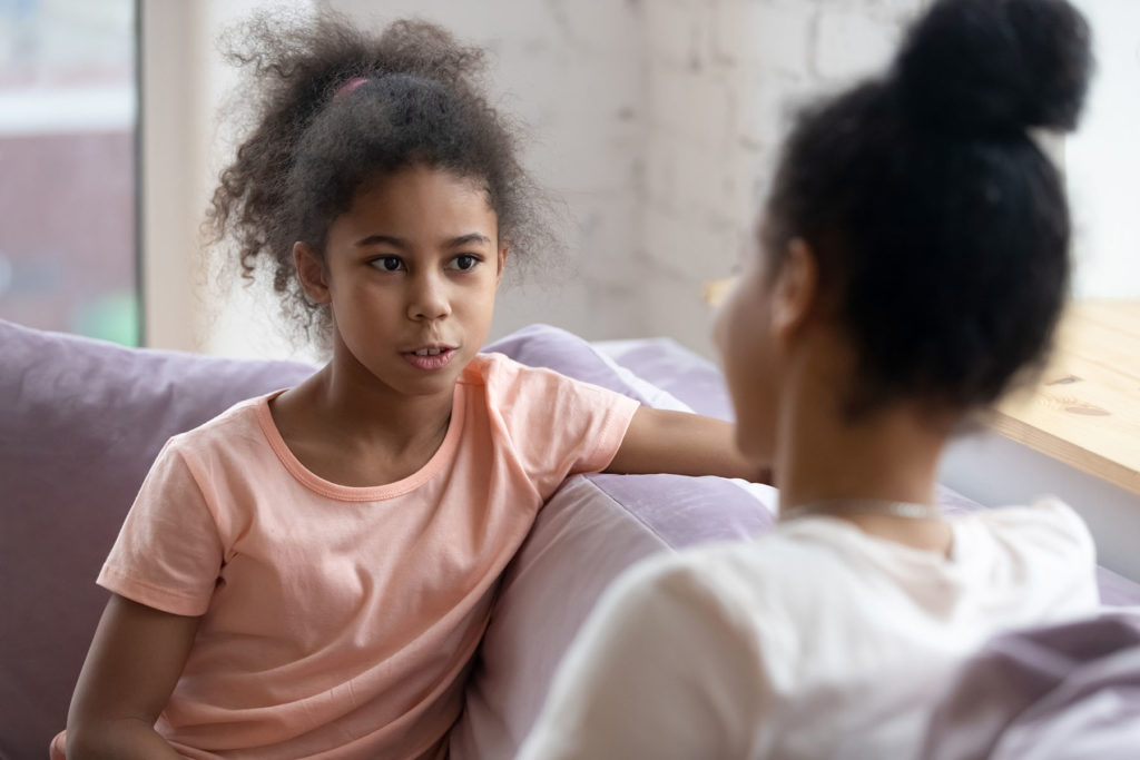 Young Black girl sits on couch having a nice talk with mother.