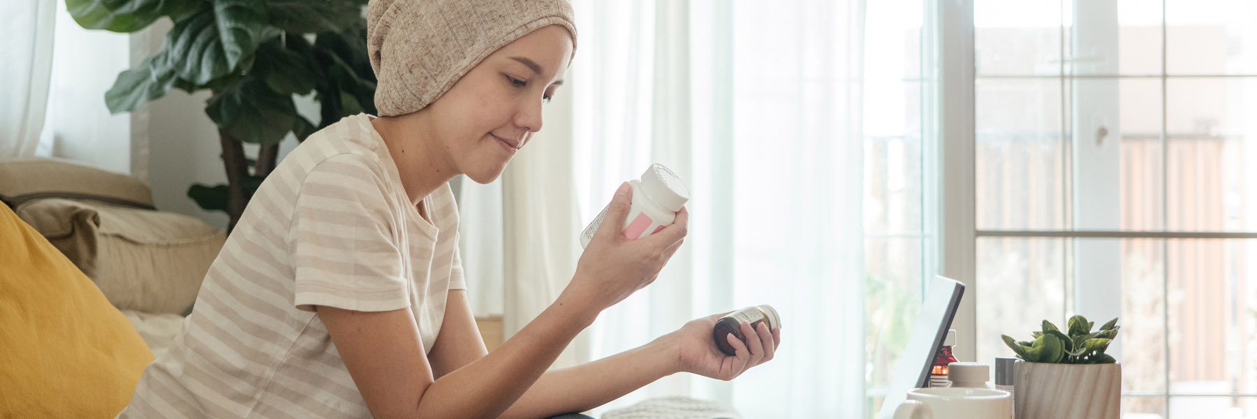 Young female cancer patient wearing a head covering reading the labels on her medication bottles