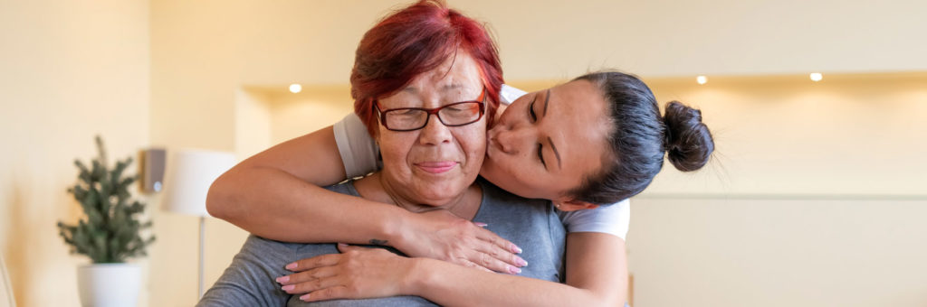 Asian woman hugging and kissing the cheek of a smiling middle-aged Asian woman