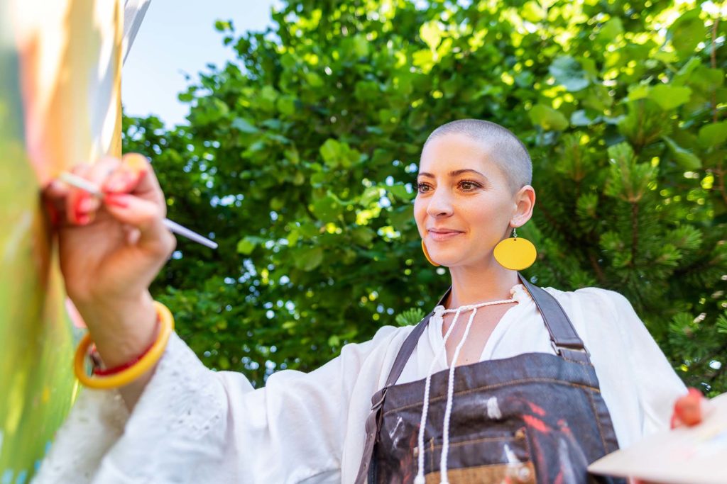 Pretty female cancer survivor paints outside as part of art therapy