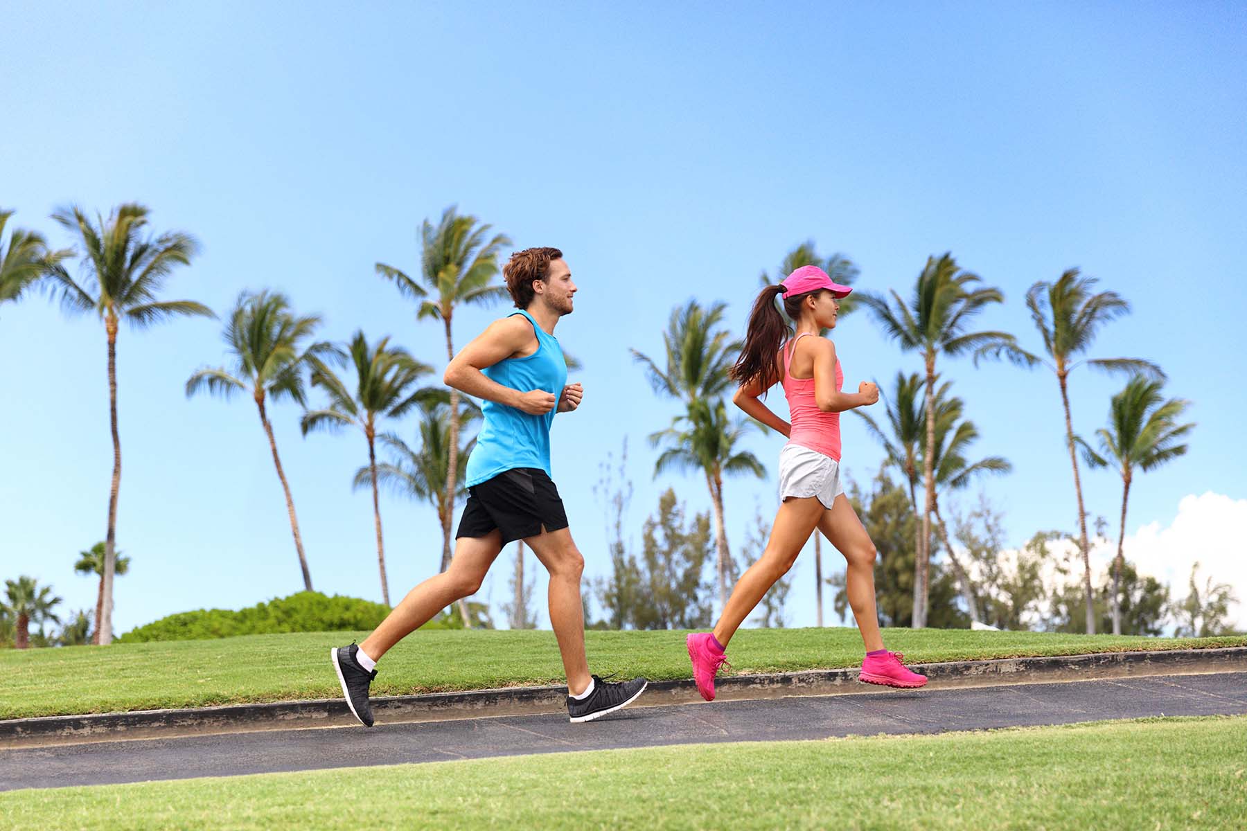 Male and female wearing athletic clothing running by palm trees