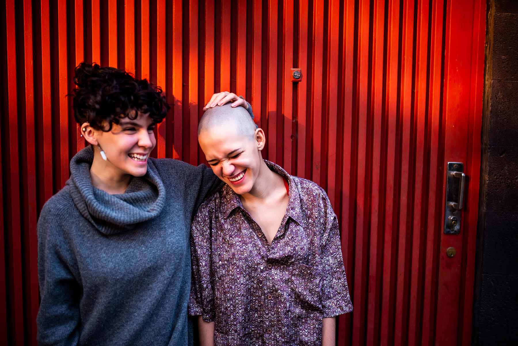 Two female friends laughing. One has cancer and smiles with her head shaved.