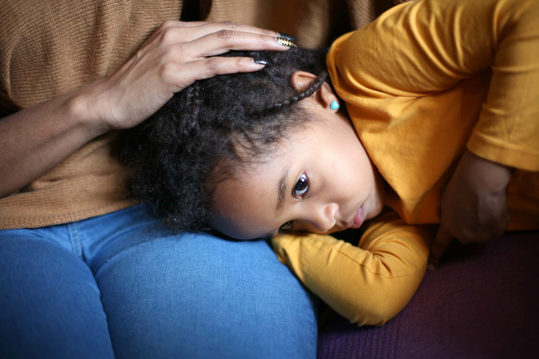 Black little girl curls up on mom's lap looking sick.
