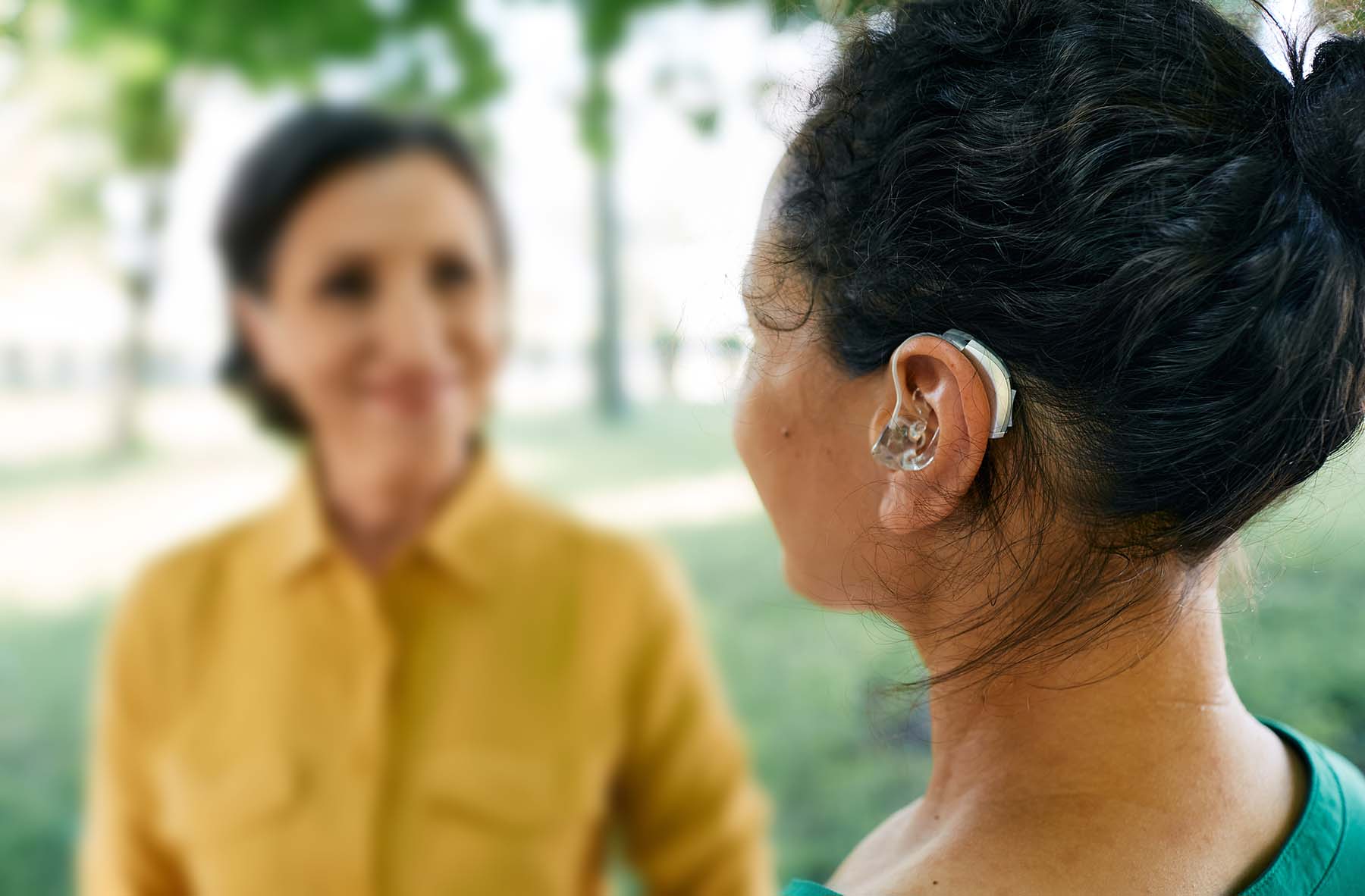 Two Hispanic women speaking outside. One is wearing a hearing aid.