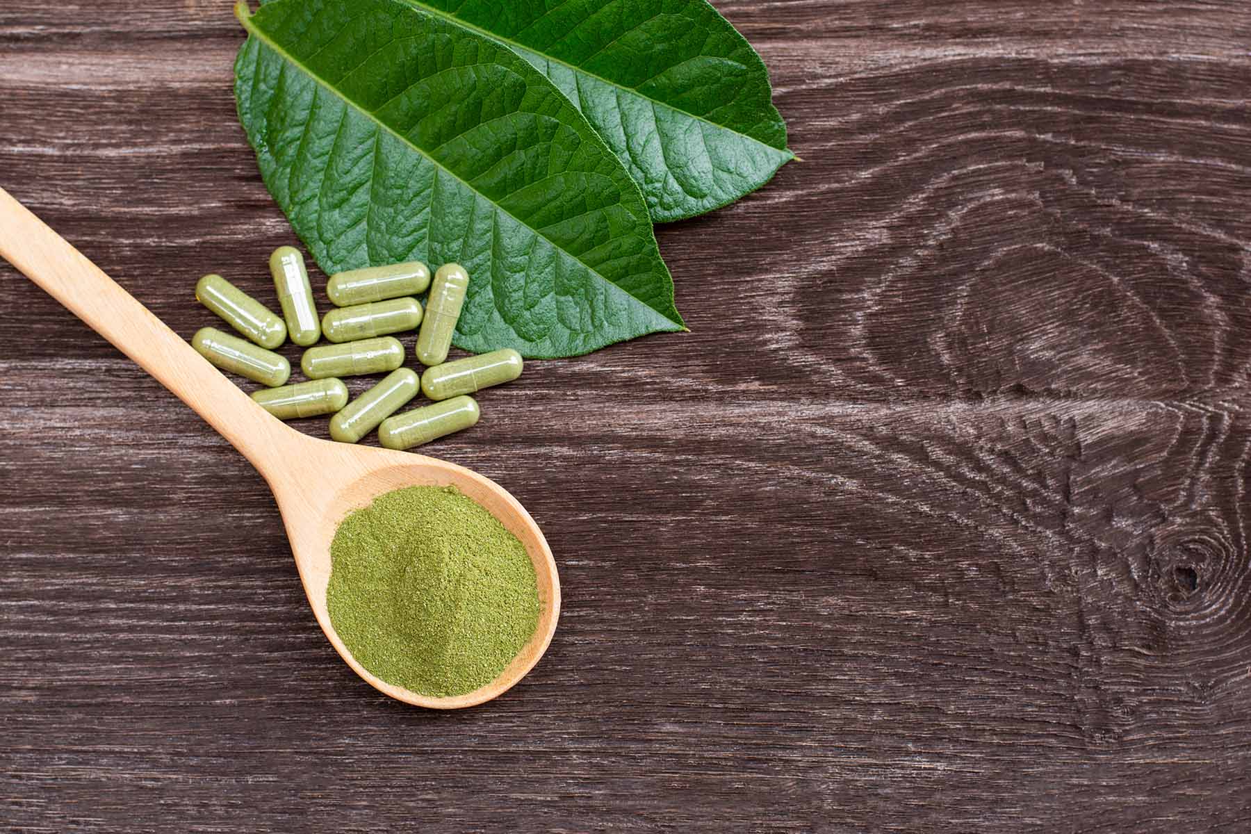 Kratom supplements and powder on a wooden backdrop