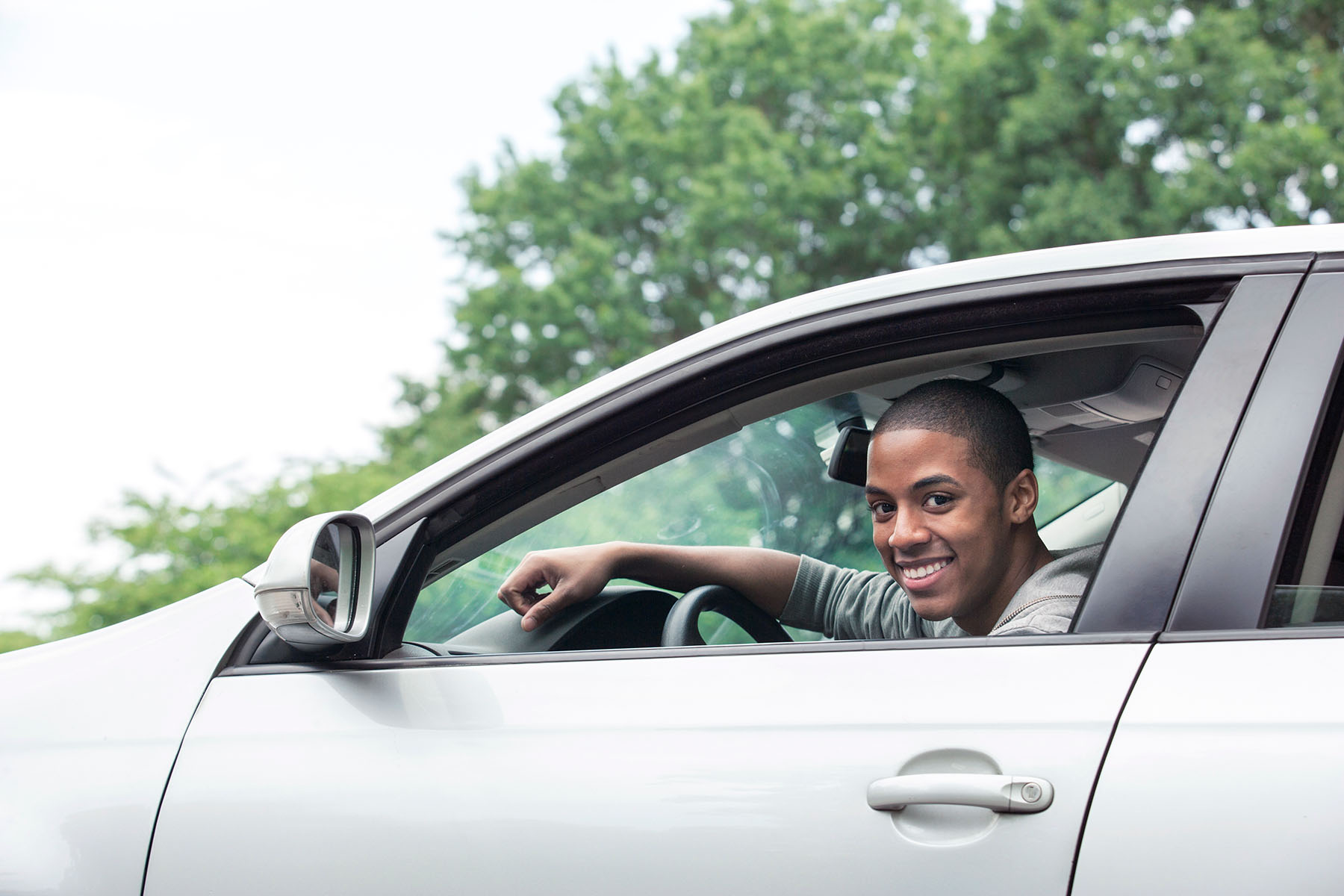 Black male teen driver smiles out the window of his sedan