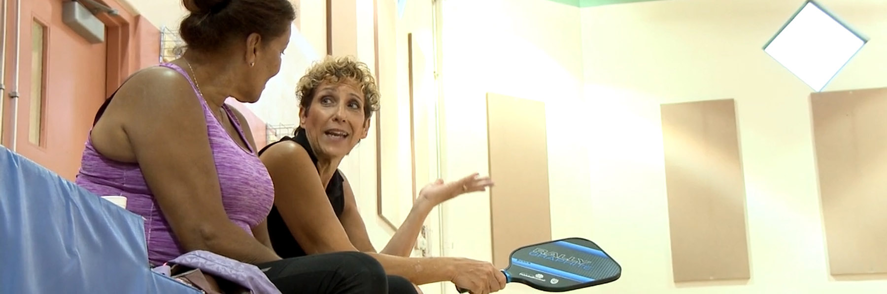 Two women take a break from pickleball to chat while holding their rackets