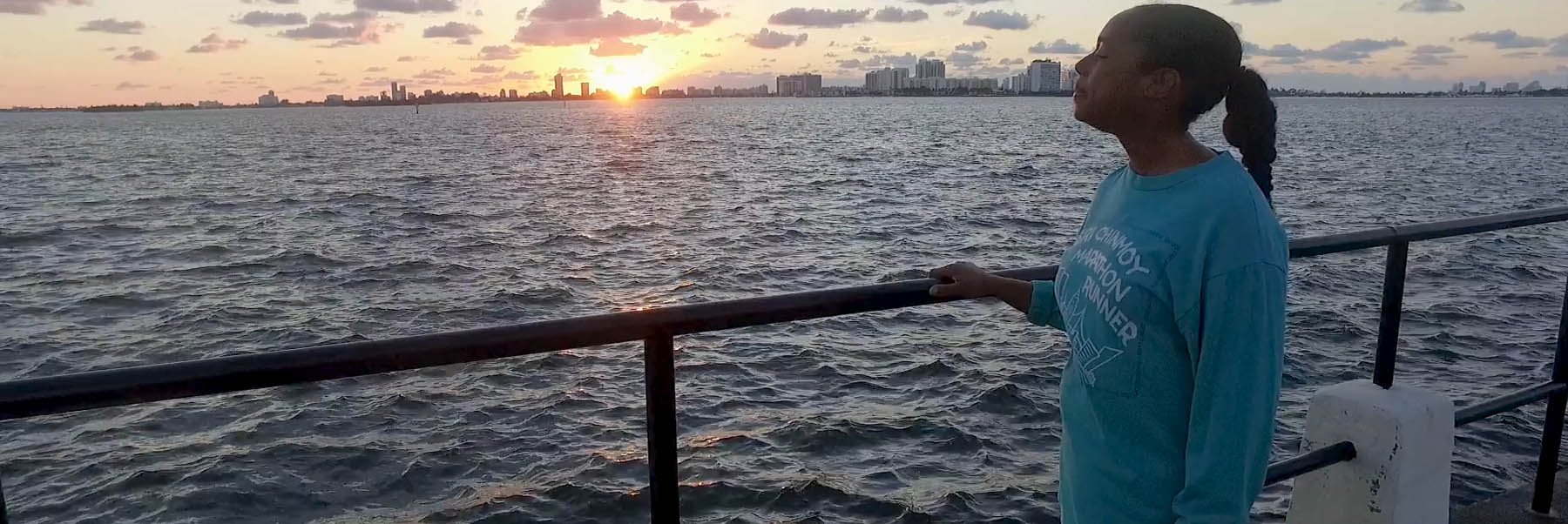 Woman looking our over the Miami intercostal waterway with the city skyline and sunset in the background