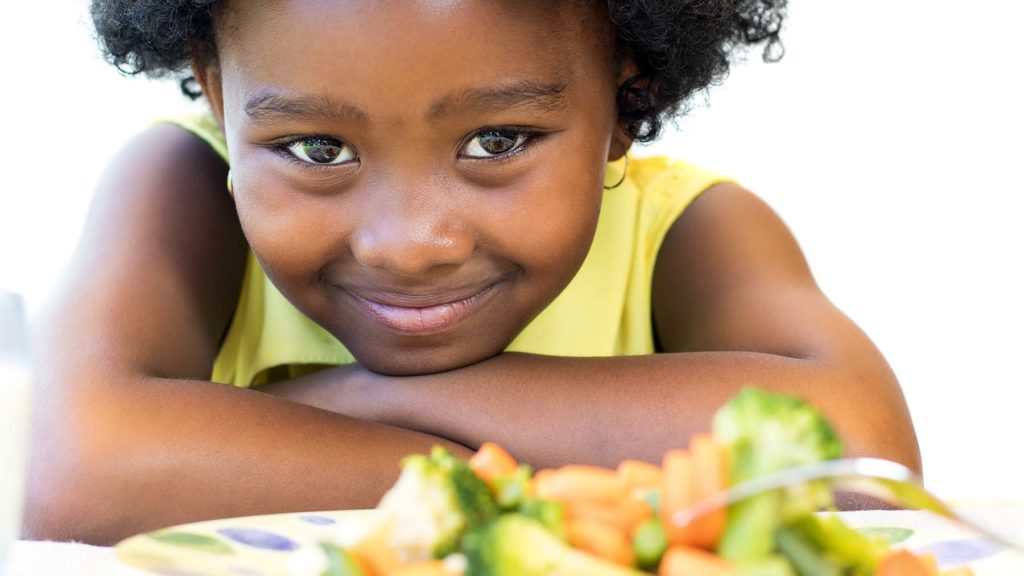 Beautiful young Black Girl smiles over a plate of vegetables.