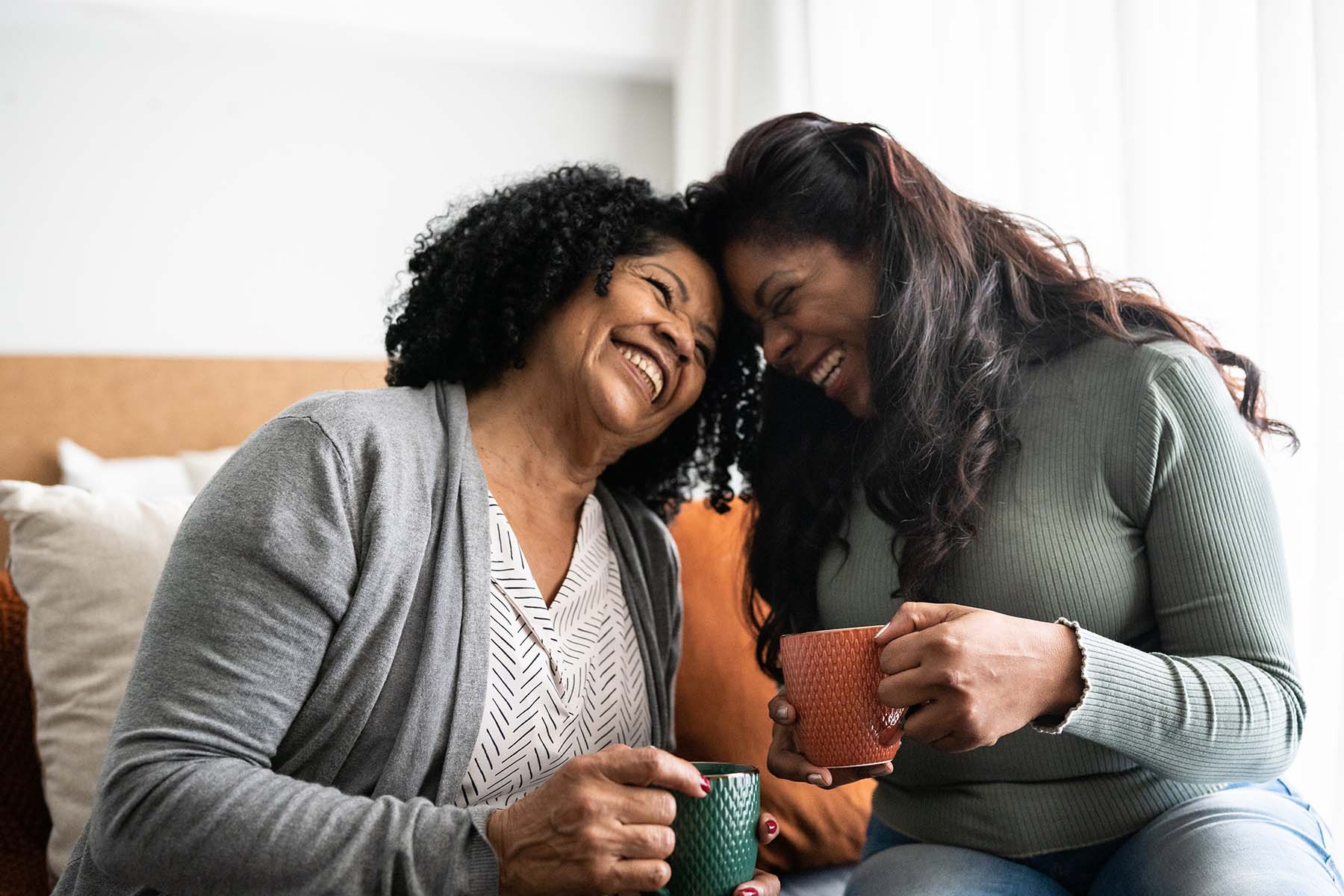 Two happy Black Hispanic women sharing a coffee on the couch.